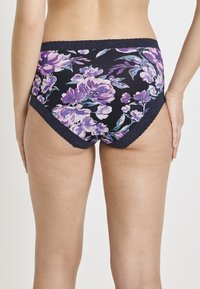 Vrouw gekleed in marineblauwe onderkleding met bloemenpatroon en kanten rand, van achteren getoond tegen een witte achtergrond.