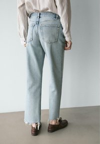 Hellblaue Jeans mit hoher Taille und geradem Bein, mit ausgefranstem Saum und klassischen Gesäßtaschen. Kombiniert mit einem gestreiften Langarmshirt und braunen Schuhen.