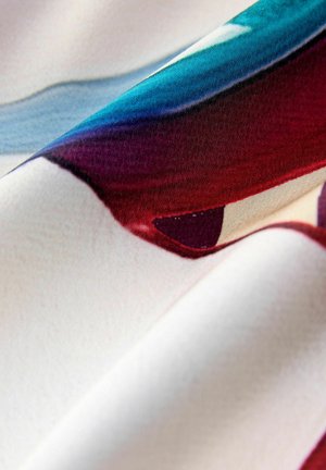 Tekstil s vibrantnim apstraktnim uzorcima u nijansama crvene, plave i krema, s glatkom teksturom i mekim padom.
