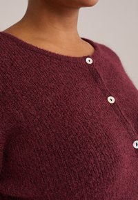 Bordeaux stickad cardigan med en texturerad väv, rund halsringning och tre vita knappar på den främre placketen. Mjuk och mysig look.