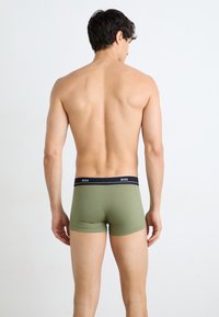 Grüne Boxer-Brief mit dehnbarem Material und einem dunklen Bund, der mit "BOSS" beschriftet ist. Mit einem enganliegenden Design und minimalistischem Stil.