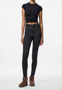 Černé krátké tričko, černé džíny s úzkým střihem a hnědé semišové kotníkové boty. Oblečení má přiléhavý střih s hladkou texturou.