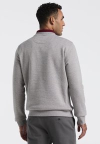 Grijze sweatshirt met een ronde hals, ribgebreide boorden en zoom. Heeft een bordeauxkleurig detail bij de kraag en een zachte, gladde textuur.