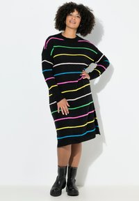 Schwarzes Strickkleid mit mehrfarbigen horizontalen Streifen (rosa, grün, blau, gelb) und lässiger Passform. Kombiniert mit schwarzen, genoppten Ankle Boots.