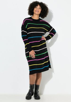 Schwarzes Strickkleid mit mehrfarbigen horizontalen Streifen (rosa, grün, blau, gelb) und lässiger Passform. Kombiniert mit schwarzen, genoppten Ankle Boots.