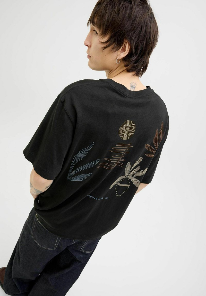 T-shirt en coton noir avec des illustrations de plantes et d'un soleil en art linéaire coloré au dos. Coupe décontractée avec des manches courtes.