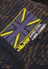 Geborduurd patch met een gestileerde Union Jack in paars en geel op een donkere textuurstof achtergrond met patroon details.