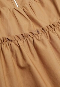 Tissu marron avec une texture froncée à la taille, présentant une finition lisse, légère et légèrement brillante. Design simple, sans motifs.