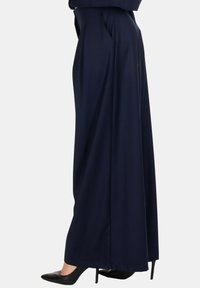 Pantaloni ampi blu navy con vita alta, pieghe e tasche laterali, realizzati in un tessuto liscio. Abbinati a tacchi a punta neri.