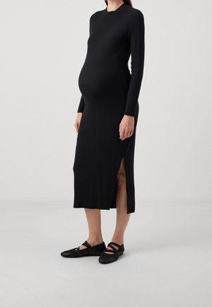 Czarna prążkowana sukienka midi z długimi rękawami, bocznym rozcięciem, dopasowanym fasonem i miękką fakturą. Połączona z czarnymi płaskimi butami z paskami.