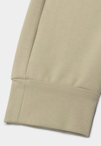 Beige sweatshirtmanchet met een geribbelde textuur en een nette afwerking. Naaddetails zijn zichtbaar, wat de zachte en flexibele stof benadrukt.