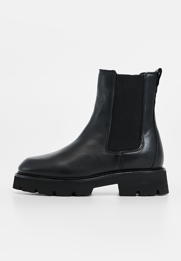 Schwarze Leder-Ankle-Boots mit elastischen Seitenpaneelen, runder Zehenform, dicke schwarze Sohle und strukturiertem Detail an den Einsätzen.