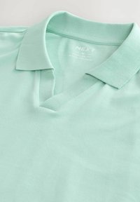 Camisa polo verde menta con un collar clásico y una apertura de cuello en V. Fabricada en tejido texturizado, presenta un diseño de corte regular.