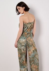 Grüner Palmenblatt-Jumpsuit mit einem trägerlosen Design, elastischem Oberteil und weitem Bein, verziert mit orangefarbenen und blauen Akzenten. Glatte Stofftextur.