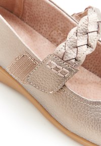 Bailarina metálica de color beige claro con una correa trenzada, parte superior de cuero texturizado y suela de goma lisa en tono marrón. Interior forrado con material suave.