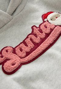Szary sweatshirt z teksturowanym, haftowanym napisem "Santa" w kolorze różowym i burgundowym, z detalem czapki Świętego Mikołaja nad napisem.