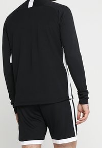 Svart träningsset bestående av en långärmad topp med vita sidostråk och shorts. Tillverkat av lätt och elastisk tyg.