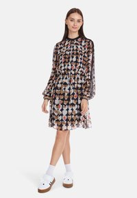 Kleid mit Gürtel aus transparenter Stoff, mit einem Herzmuster in Creme, Braun und Rot auf einem marineblauen Hintergrund. Lange Ärmel mit elastischen Bündchen.