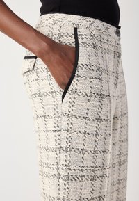 Pantaloni bianchi di tessuto con un motivo a quadri neri, caratterizzati da dettagli sulle tasche neri a contrasto e una silhouette aderente.