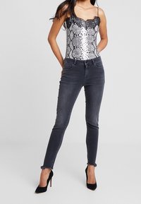 Silverfärgad ormtryckt bodysuit med spetsdetaljer, ihopparad med mörkgrå skinny jeans med rå fåll, kompletterad med svarta högklackade skor.