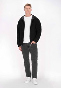 Svart zip-up hoodie med grå innerfoder, bärs över en vit t-shirt. Kombineras med slim-fit grå jeans och vita sneakers.