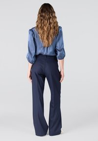 Lichtblauwe satijnen blouse met puffed sleeves, gecombineerd met donkerblauwe gestreepte broek. De outfit heeft een getailleerde taille en een vloeiende pasvorm.