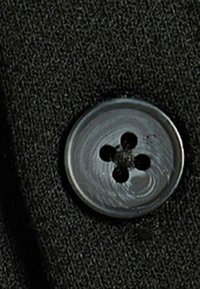 Pulsante nero con quattro fori, superficie liscia e leggero lucido, attaccato a uno sfondo di tessuto nero textured.