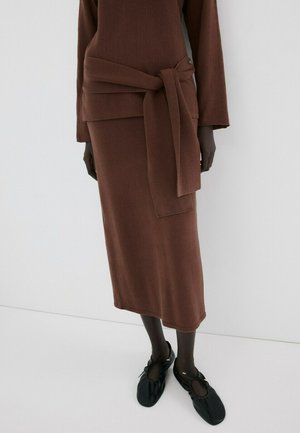 Falda midi de punto marrón con top a juego que incluye un cinturón ancho anudado, combinado con zapatos planos negros de cuero suave y cordones.