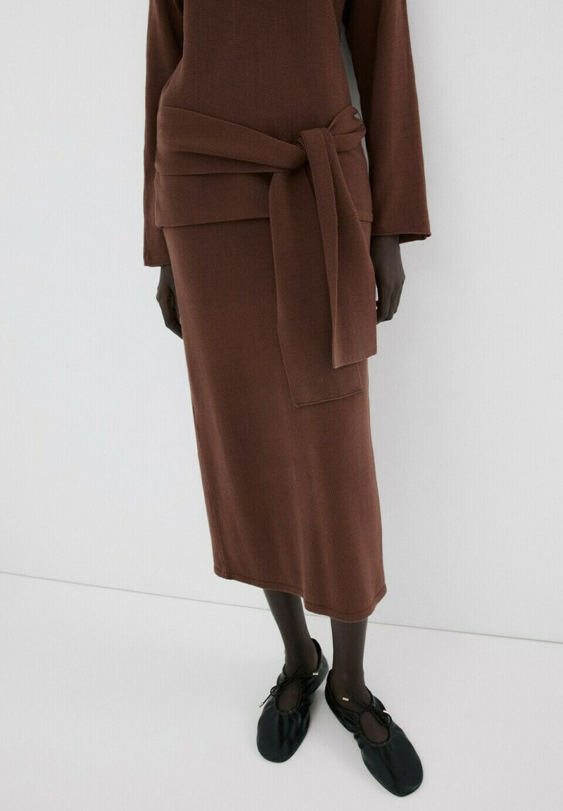 Brauner Strick-Midirock mit passendem Oberteil, das einen breiten gebundenen Gürtel trägt, kombiniert mit schwarzen flachen, weichen Leder-Schnürschuhen.