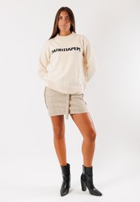 Maglione crema con lettering nero "PATRIZIA PEPE", abbinato a una mini gonna a quadri beige e stivaletti neri con tacco alto.
