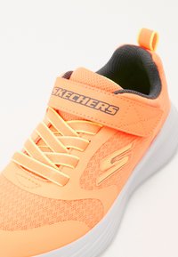 Orange athletic sneakers with textured mesh upper, white sole, and Velcro strap, featuring logo and laces in matching color.