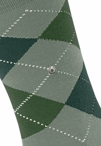 Calzino argyle verde con motivi a rombi in diverse tonalità di verde e grigio, con cuciture bianche e un accento metallico rotondo.