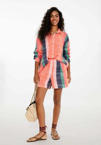 Živo farebný pruhovaný outfit s košeľou na gombíky s dlhým rukávom a zodpovedajúcimi šortkami v ružovej, zelenej a námorníckej modrej farbe. Hladká textúra látky.