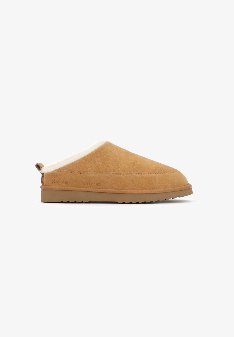 Pantofii slip-on din suede bej, cu un interior moale din blană, talpă plată din cauciuc și branding subtil pe lateral. Design simplu, fără hardware vizibil.