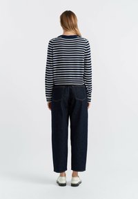Maglietta a righe navy e bianca a maniche lunghe abbinata a pantaloni in denim scuri a vita alta e scarpe slip-on bianche. Look semplice e casual.