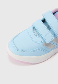 Zapatilla deportiva azul claro con correas ajustables de Velcro, materiales de cuero y malla, suela blanca con acento rosa, superficie texturizada y detalles plateados.