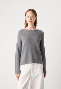 Grijze gebreide trui met een ribbelstructuur, wijd decolleté en lange mouwen. Draagt met witte broek, met een relaxte pasvorm en eenvoudig ontwerp.