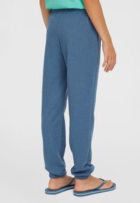 Pantaloni sportivi blu realizzati in tessuto morbido, con un elastico in vita e orli a costina. Abbinati a ciabatte blu.