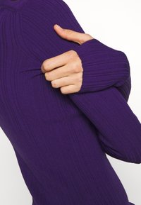 Lila ribbad långärmad topp med åtsittande manschetter. Tyget har en texturerad yta med vertikala ränder, vilket betonar en tight silhuett.