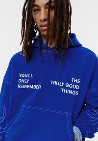Blauwe hoodie van katoen met witte tekst: "YOU'LL ONLY REMEMBER" en "THE TRULY GOOD THINGS." Heeft een voorzak.