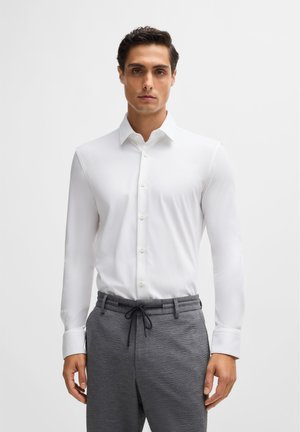 White long-sleeve shirt with a button-down collar, paired with gray textured pants featuring an elastic waistband and drawstring.