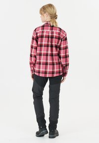 Rosa und schwarze karierte Flanellhemd mit geknöpften Manschetten, kombiniert mit dunklen, eng anliegenden Hosen. Die Schuhe sind schwarz mit einer strukturierten Sohle.