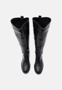 Μαύρες δερμάτινες μπότες μέχρι το γόνατο με λείο φινίρισμα, στρογγυλεμένη μύτη και στρογγυλεμένη κορυφή. Διαθέτουν μικρό πλαϊνό φερμουάρ και θηλιά έλξης.