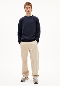 Marineblauwe sweatshirt met ronde hals, beige broek met diagonale naden en grijze sneakers met zwarte accenten. Eenvoudig, functioneel ontwerp.