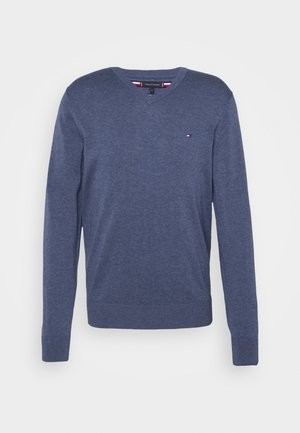 Granatowy sweter z długim rękawem i dekoltem w serek, z małym czerwono-biało-niebieskim logo na lewej stronie klatki piersiowej oraz ściągaczami na mankietach i u dołu.