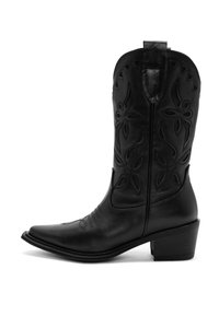 Bota vaquera de cuero negro con puntera afilada, costuras detalladas, patrones de corte en forma de flor y un tacón en capas.