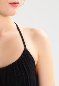 Svart ärmlös topp med tunna band, med en plisserad textur och rundad deco, som visar en mjuk tygkonstruktion och en figurnära design.