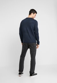 Navy trui met geribbelde kraag en zoom, gecombineerd met donkergrijze broek en zwarte sneakers. De trui heeft een textuur gebreid ontwerp.