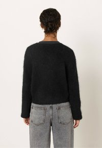 Svart, fluffig tröja med avslappnad passform och långa ärmar, kombinerad med högmidjade, ljusgrå jeans med bakfickor.