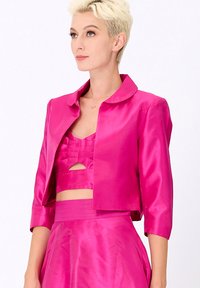 Veste cropped en satin rose avec un col, des manches trois-quarts et une texture lisse. Portée par-dessus un top cropped assorti avec des découpes.